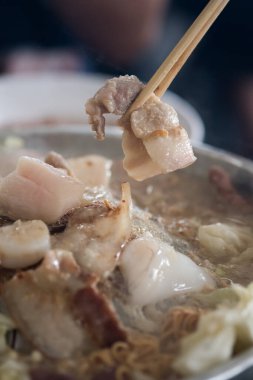 Yemek için domuz eti dilimlerini tencereden toplamak için çubuk kullan. Domuz göbeğine odaklan.