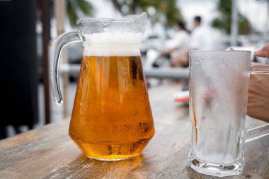 Açık hava restoranında dondurulmuş cam bardakların yanında içi taze bira dolu cam bardak.