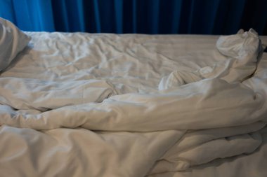 Yatağında battaniyesi olmayan beyaz bir yastık. Sabahtan sonra rahatlama kavramı. Işıklandırma penceresi ve mavi perdesiyle.