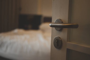 Lüks bir otelde kilitli bir kapı kolu ve odasının ahşap panelli kapısı, yatak ve yastıkların arka planı.