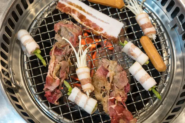 Raw beef and bacon roll with enoki mushroom and vegetable on yakiniku stove which has hot charcoal. Barbecue Japanese style. Yakiniku. Is the Japanese version of Korean BBQ. Barbecue grilled on stove.