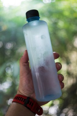 Su şişesini doğaya karşı tutan adam yeşil arka plan