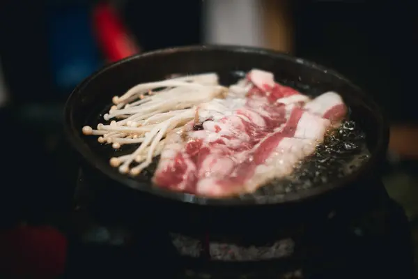 Cooking raw beef and golden needle mushroom on grilled meat on hot pan. Close up