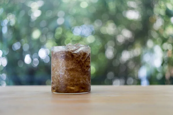 Glass of soft drink with iced on wood table against nature background