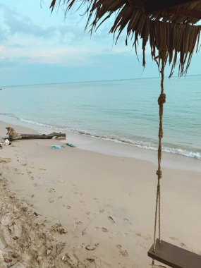 Mavi denizde ve plaj arka planında boş ahşap salıncak. Akıllı telefonla fotoğraf çek.