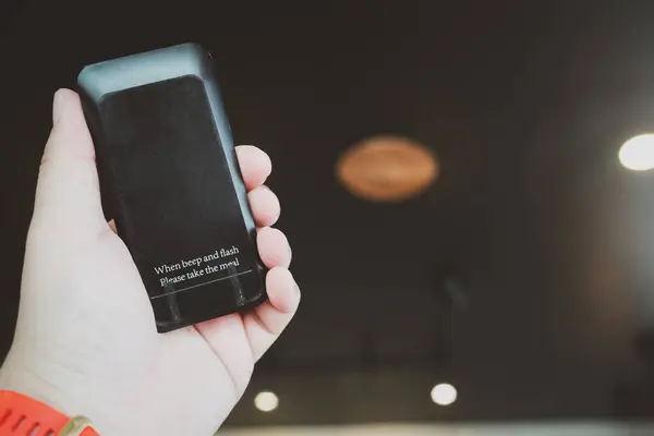 Hand holding black queue paging Wireless Calling System for restaurants, coffee shops or cafe