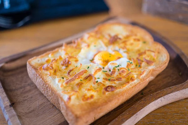 Cheesy baked egg toast served on wooden board, close up