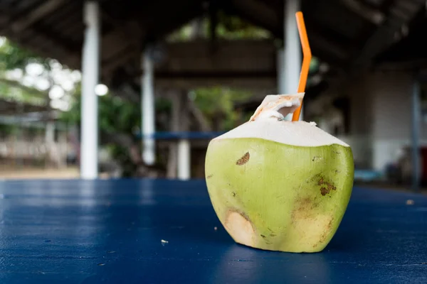 Coconut fruit drink with a orange plastic straw. Fresh coconut drink on blue wood table. Real coconut drink