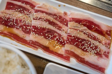 Çiğ domuz dilimleri. Beyaz tabakta beyaz susam tohumlarıyla marine edilmiş..