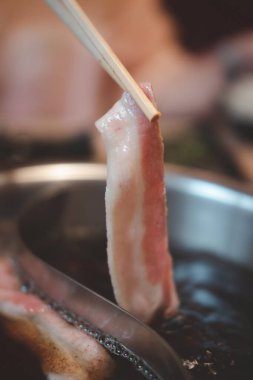 İnce dilimlenmiş çiğ domuz pastırması, shabu-shabu domuz eti, çubuklar domuz dilimlerini topluyor.