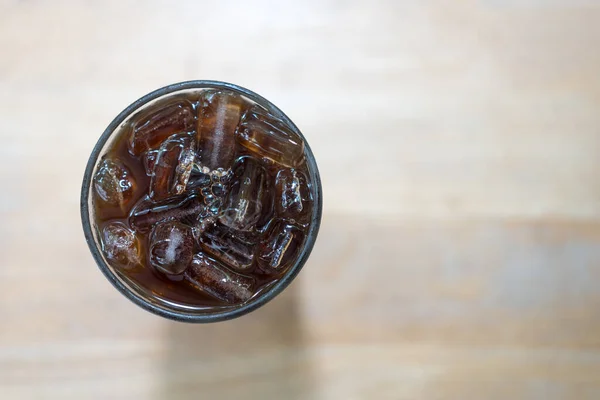 A glass of ice black coffee on wood table. Top view