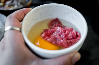 Haşlanmış Japon Sukiyaki için çiğ yumurta içine taze et konmuş.