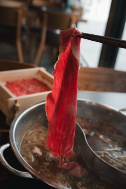 Japon Shabu restoranında bir parça haşlanmış çiğ etle yemek çubuğu tutan bir adam.