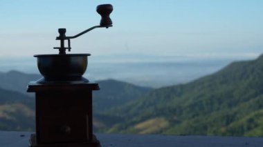 Kahve öğütücüsü ahşap sehpanın üzerinde, doğal arka planda, sabahları kahve zamanı dağ manzaralı ve doğal yeşil manzaralı soğuk ve rahat.