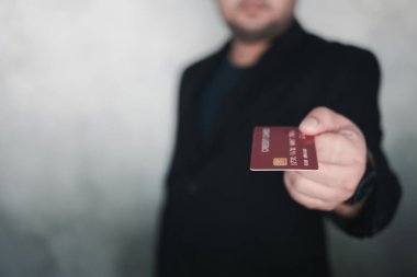 A young businessman in a black suit standing holding a credit card to pay for online shopping, application for purchases, finance, and banking