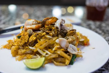 Pat Thai, tofu, sebze, yumurta ve beyaz tabakta bir sürü deniz ürünüyle kızartılmış ince pirinç eriştesi. Geleneksel Tayland Kızarmış Eriştesi