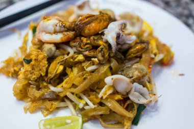 Pat Thai, tofu, sebze, yumurta ve beyaz tabakta bir sürü deniz ürünüyle kızartılmış ince pirinç eriştesi. Geleneksel Tayland Kızarmış Eriştesi