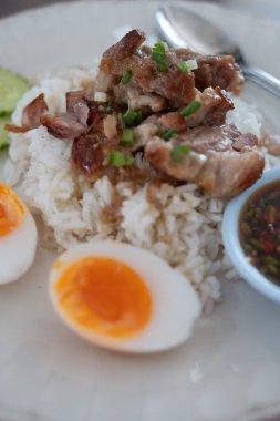 Haşlanmış yumurta ve dilimlenmiş salatalıkla servis edilen haşlanmış pirincin üzerine konmuş domuz eti dilimi.