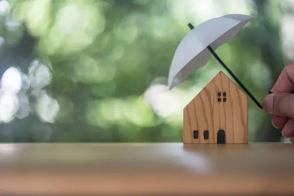 Home and real estate insurance ideas, Man use white small umbrellas and wood homes. Home insurance for upcoming losses and fires building fire insurance. Insurance is risk control
