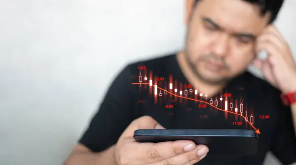 Man using mobile phone checking stock market graph report via mobile apps trading decreasing chart data fall down. Upset by fall in value shares. Decline in share price. Losing money on stock exchange
