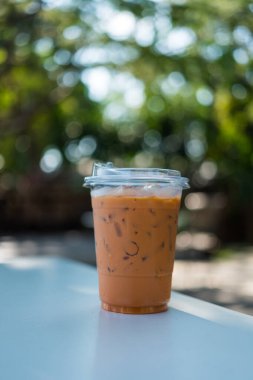 Tahta masadaki plastik bardaktaki buzlu Thai sütlü çay doğal bir arka plana karşıdır. Tayland içeceği..
