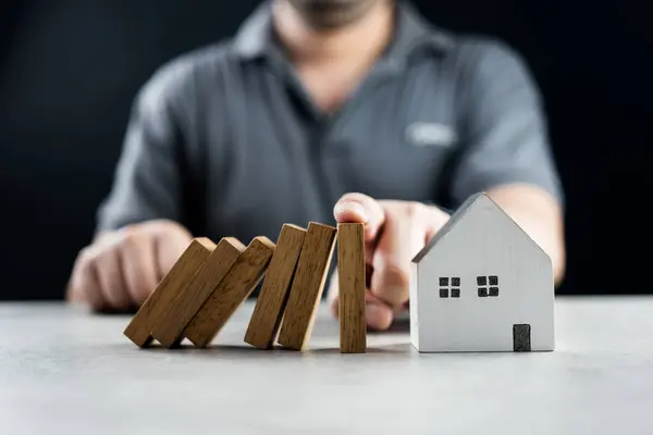 Man hand stopping risk the wooden blocks from falling on house, Investment risk and uncertainty in the real estate housing market, insurance. Risk control concept. Risk plan real estate protection