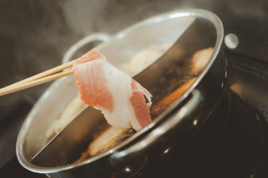 Erkek eli çiğ, lezzetli, kaliteli domuz dilimleri alıyor. Restorandaki sebzeli sıcak kaynamış çorbanın içine koyuyor..