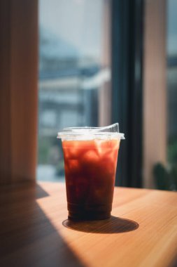 Güneş ışığıyla kaplı ahşap masanın üzerinde duran plastik bardak.