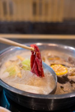 Bir çift el sıcak kaynatılmış etin içine ince dilimlenmiş et konulmuş odun çubukları kullanır. Japon shabu shabu sukiyaki