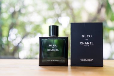 Bangkok, Tayland - 10 Temmuz 2024: Erkekler için bir şişe parfüm Bleu de Chanel doğaya karşı ahşap masa üzerine yerleştirildi