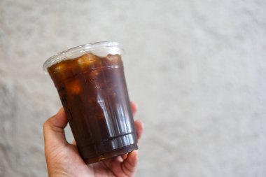 Elinde plastik bardak buzlu Ameracano kahvesi tutan birinin kırpılmış görüntüsü.