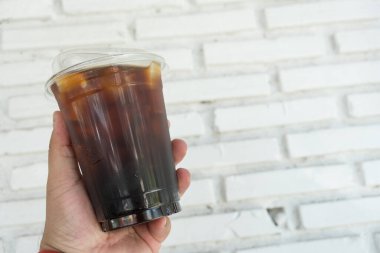 Elinde plastik bardakta buzlu americano.