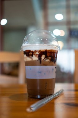 Ahşap masadaki bir kafede plastik bir fincanda buzlu kahve.