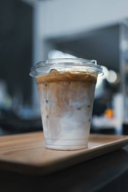 Kafedeki ahşap tepside plastik bardakta buzlu latte. Kapat.