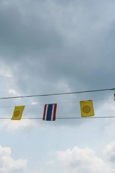 stock image Thai Dharmachakra Buddhist flags and Thai nation flags waving in the air uder blue sky