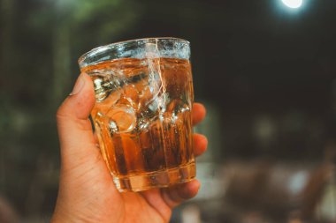 Buzlu viski bardağı tutan adam, arka plan bulanık.