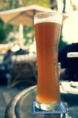 Açık hava restoranının masasında duran uzun, bükülmüş bir bardakta light bira.