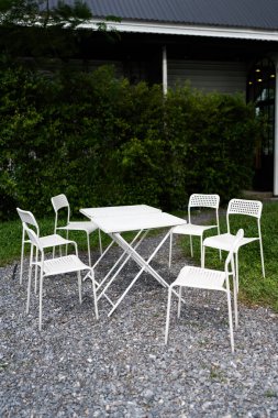 Bahçe avlusunda beyaz sandalye ve masa.