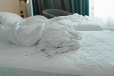 Beyaz kırışık battaniye yastık yapılmamış yatakta sabah güneşi pencereye vuruyor.