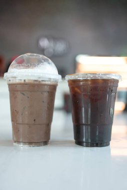 Buzlu Americano kahvesi ve buzlu kahve. Kahve dükkanındaki beyaz masada plastik kahve fincanı.
