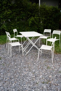 Bahçe avlusunda beyaz sandalye ve masa.