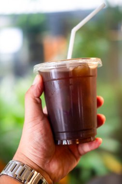 Plastik bardakta buzlu Amerikan kahvesi. Bokeh doğa ışığıyla.