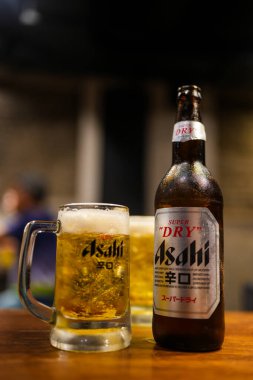 Bangkok, Tayland - 26 Ekim 2024: Asahi bira şişesi ve ahşap bir masada köpüklü Asahi birası