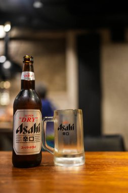 Bangkok, Tayland - 26 Ekim 2024: Ahşap masada Asahi bira şişesi ve bira bardağı