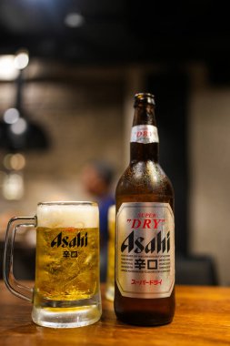 Bangkok, Tayland - 30 Ekim 2024: Asahi bira şişesi ve ahşap masada köpüklü Asahi birası