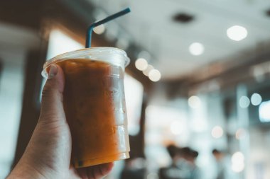 Kafe arka planında buz ve portakal suyuyla karıştırılmış bir bardak soğuk kahve tutuyor. Seçici odak