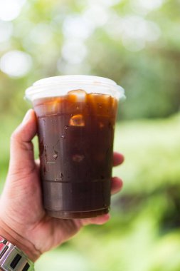 Buzlu americano plastik cam ellerde bahçe arka planı ve bokeh ışığı var.