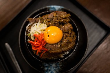 Wagyu bifteği pilavı ve çiğ yumurta kasesi, kremalı yumurta sarısı leziz bifteği kucaklıyor, dokuların ve tatların lezzetli bir harmonisine karışıyor siyah bir kasede..