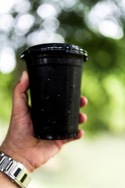 Elinde plastik bir fincan buzlu kahve tutan bir adamın yakın plan fotoğrafı..