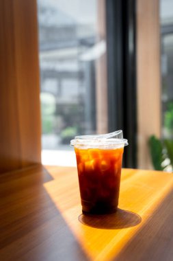 Güneş ışığıyla kaplı ahşap masanın üzerinde duran plastik bardak.